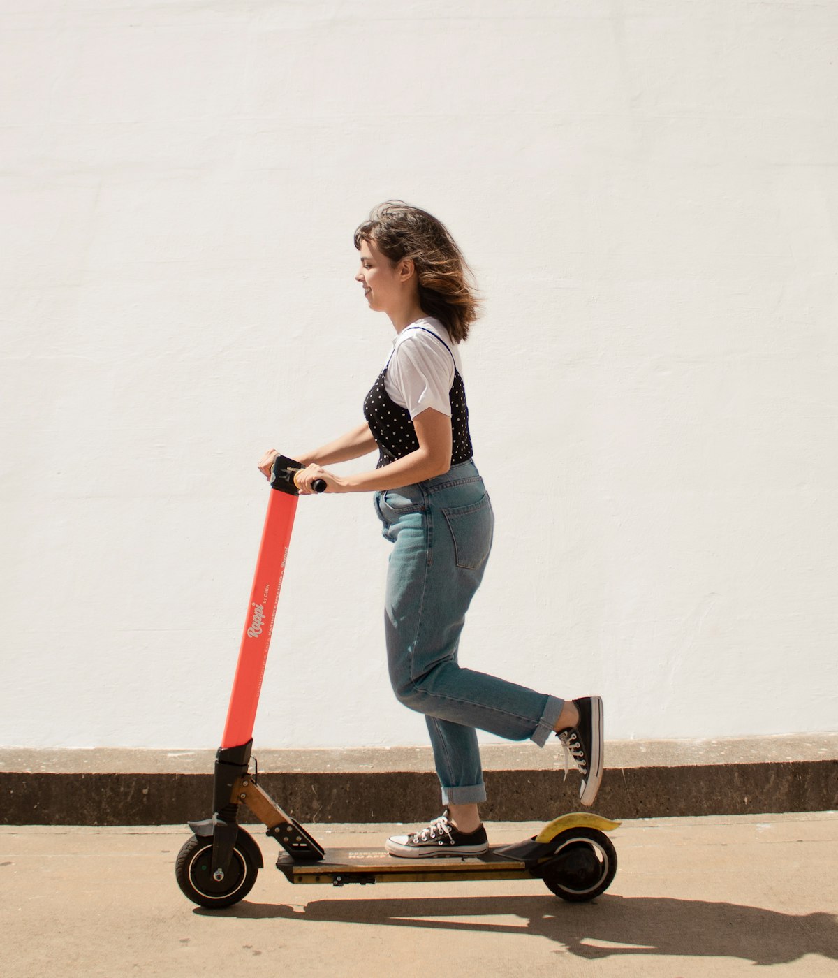 Femme sur une trottinette électrique devant un mur clair